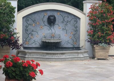 A fountain in a garden with red flowers.