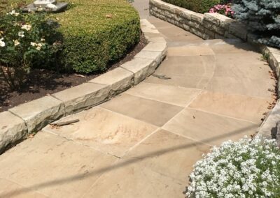 A stone walkway in a garden with flowers and plants.